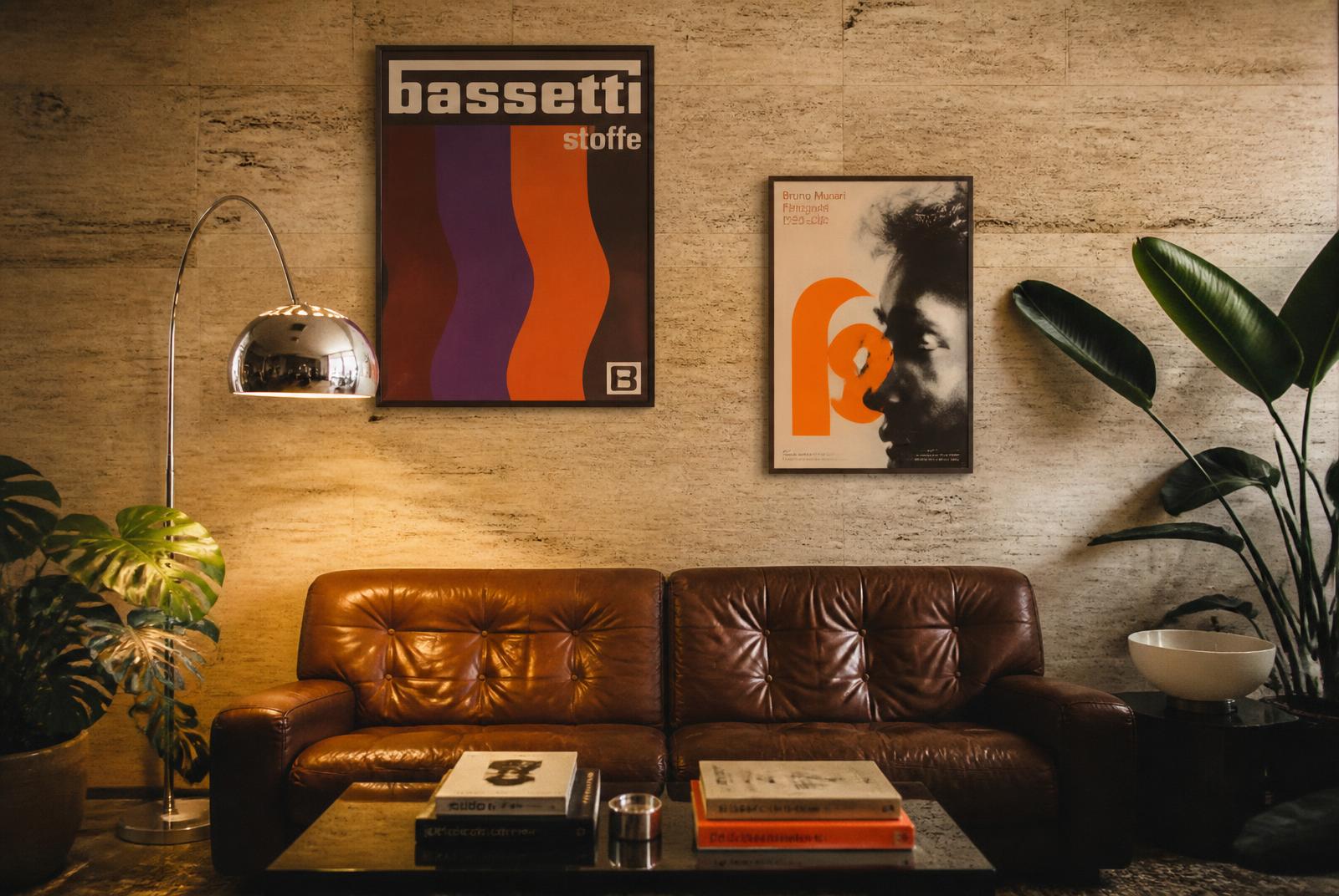 Mur en travertin d'un studio créatif avec deux affiches graphiques encadrées, canapé en cuir brun et lampe arc chromée