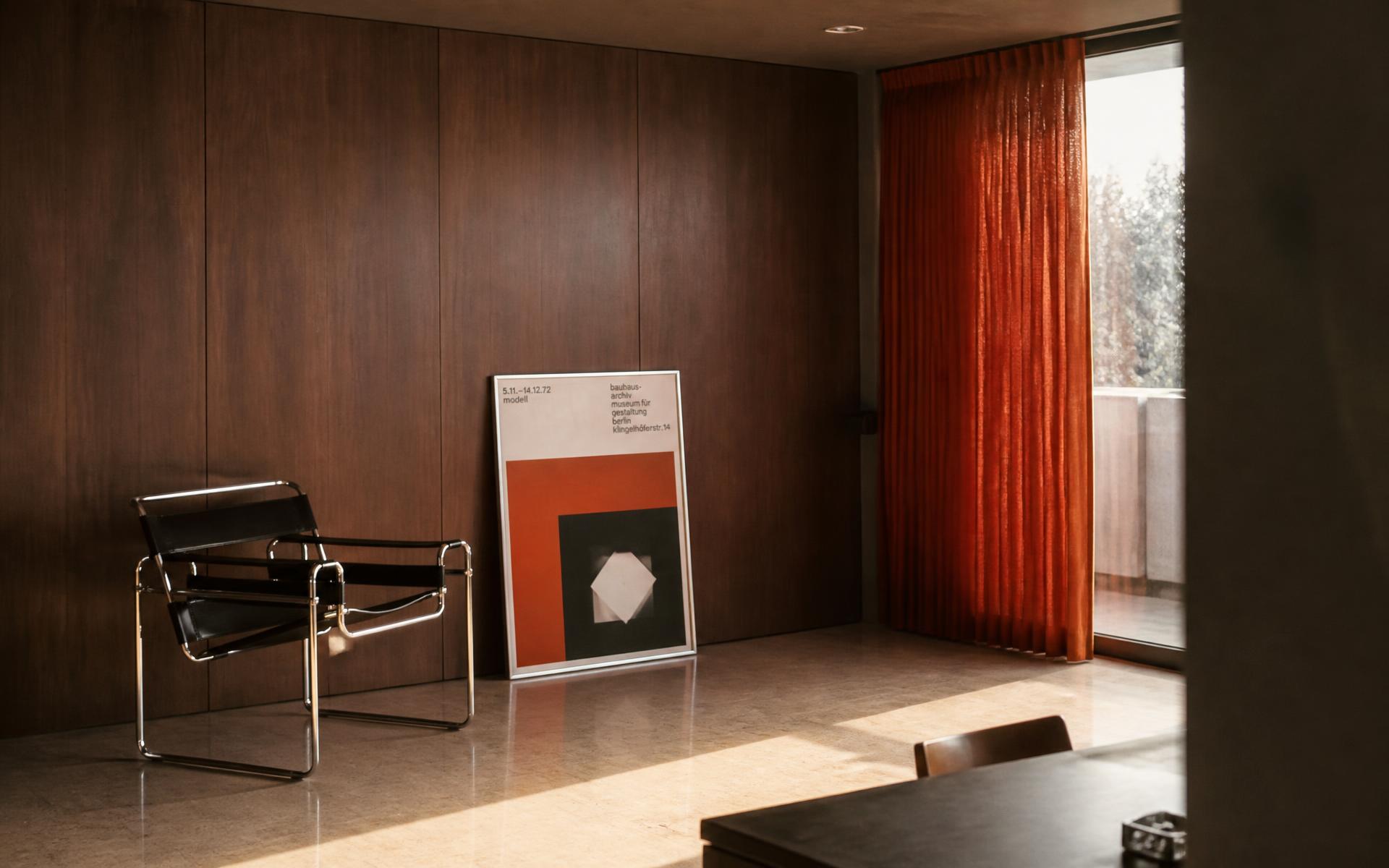 Salon d'appartement d'architecte des années 70 : boiseries sombres, sol en travertin, fauteuil chromé et affiche graphique encadrée